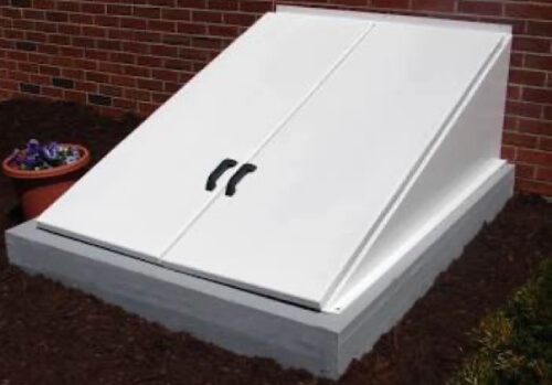 White basement walkout hatchway installed against a brick foundation